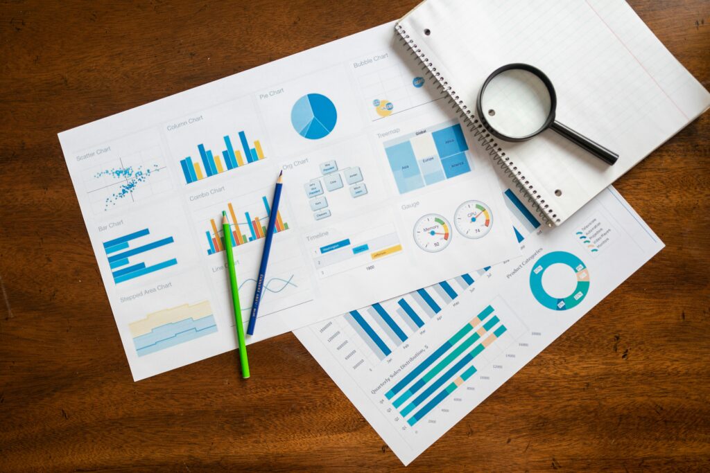 Overhead view of financial charts, magnifying glass, and stationery on wooden table.